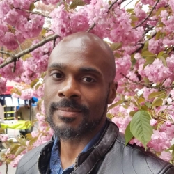 A black man standing outdoors in front of flowers